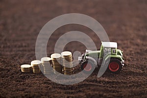 Tractor miniature with coins on fertile soil land