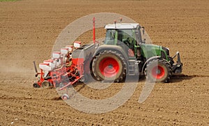 Tractor with a modern sowing seeds machine in a newly plowed field in springtime. Side view. Plowed land on background