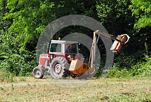 Tractor mounted hydraulic brush cutter at work in a summer day