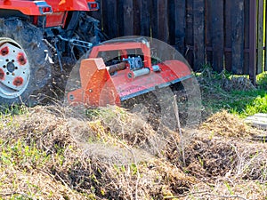 A tractor with a mower attached mulches dry grass along the fence. Land plot processing