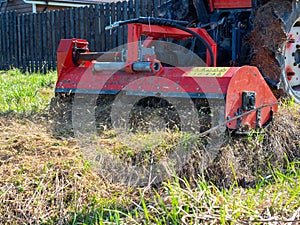 A tractor with a mower attached mulches dry grass along the fence. Land plot processing