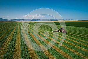 Tractor mowing green agriculture field, aerial drone view