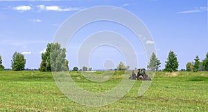 The tractor mows the grass in the meadow. Haymaking in the countryside.