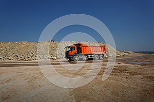 An orange dump truck, lorry full of stones in a sand quarry, transporting of materials on a natural background.