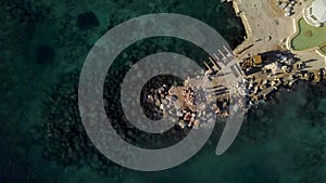 Tractor performing construction works on a dam in the sea. Above view of breakwater