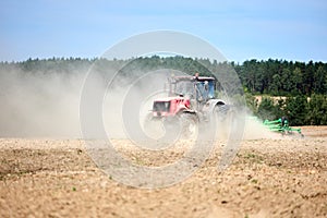 Tractor is plowing field with harrow. Typical agricultural scene tractor cultivation in field in clouds of dust