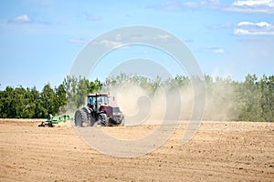 Tractor is plowing field with harrow. Typical agricultural scene tractor cultivation in field in clouds of dust