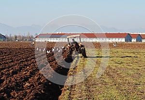 Tractor plows the field in front of some agricultural buildings