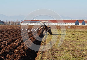 Tractor plows the field in front of some agricultural buildings photo