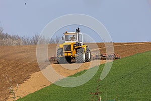 A tractor plows a field with seedbed cultivator in early spring