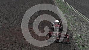 The tractor plows the ground on the field at the beginning of the planting season. A farmer stands on the tracks of his