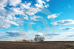 Tractor plows the large soil field against blue cloudy sky background