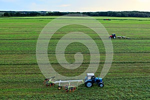 Tractor raking grass for silage harvesting. Agriculture machinery working at field. Grass Silage for animal feeding on the farm.