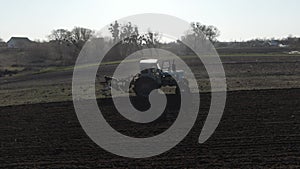 Tractor riding backward along furrows on sundown. Wide shot of agricultural machinery working on rural field on sunset