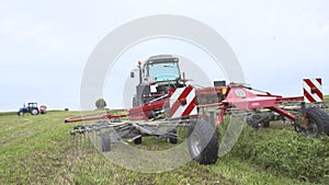 Tractor riding on farm field with combine carriage cutting grass