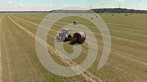 Tractor with a roll baler collects hay in bales on a Sunny hot day in summer