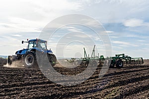 A tractor with seedbed cultivator ploughs field on morning