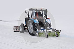 Tractor with a snow plow and a mechanical sweeper moves on a snowy background