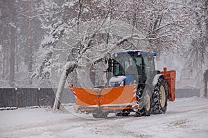 Tractor with a snow shovel attachment driving down a street in winter.