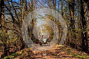 tractor on soil road in spring forest against blue sky