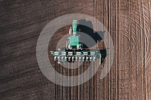 Tractor sows plowed soil on farm field, spring agriculture, aerial view from drone