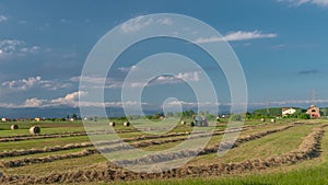 A tractor with special machinery runs through a field covered with dry grass to produce large bales of hay