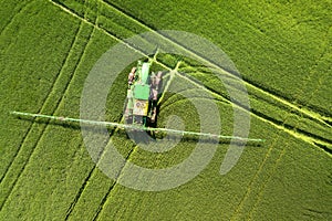 Tractor spraying chemical pesticides with sprayer on the large green agricultural field at spring