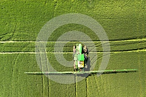 Tractor spraying chemical pesticides with sprayer on the large green agricultural field at spring