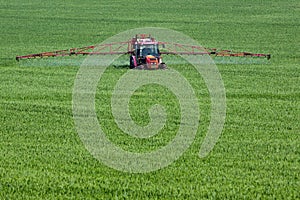 Tractor spraying pesticides on big green field