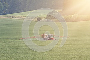 Tractor spraying pesticides on big green field