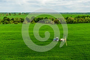 Tractor spraying pesticides on wheat field with sprayer at spring