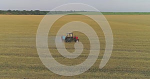 The tractor sprays the wheat fields. Spraying a field with wheat view from a drone. A tractor sprays wheat with