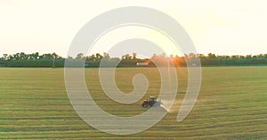 The tractor sprays the wheat fields. Spraying a field with wheat view from a drone. A tractor sprays wheat with