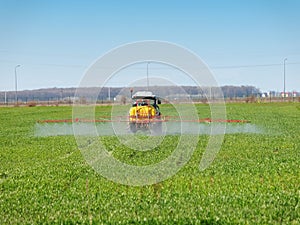 Tractor spreading herbicides over a green field