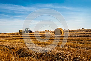 A tractor with trailed bale machine collect straw in the field