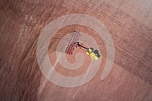 A tractor with a trailed cultivator works on a red earth arable land. Shooting from the air. Copy space