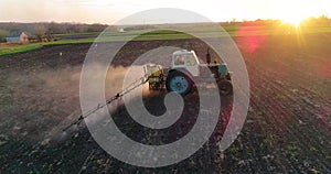 Tractor with trailed sprayer spraying chemicals on agricultural field. Aerial view