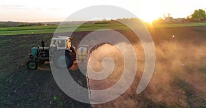 Tractor with trailed sprayer spraying chemicals on agricultural field. Aerial view