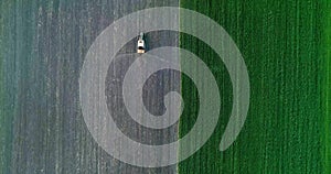 Tractor with trailed sprayer spraying chemicals on agricultural field. Aerial view