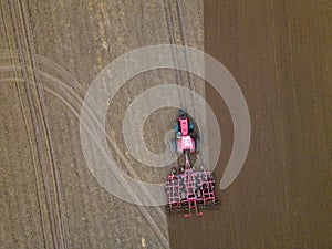 A tractor with a trailer plough plows a farmer's field from a aerial view. Top view of working rural machinery