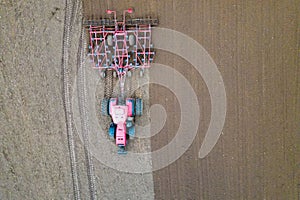 A tractor with a trailer plough plows a farmer's field from a aerial view. Top view of working rural machinery