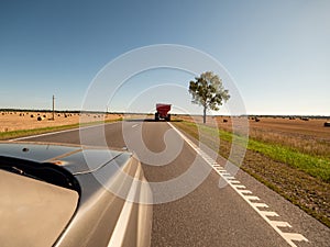 Tractor with trailer on a road by a big agriculture field. Warm sunny day with blue cloudy sky. Food supply chain. Grain product