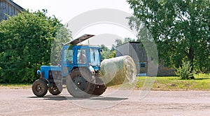 The tractor transports twisted sheaf hay, straw rolls in the trailer of the agricultural machine