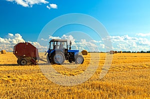 A tractor uses trailed bale machine to collect straw in the field and make round large bales. Agricultural work, baling
