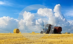 A tractor uses trailed bale machine to collect straw in the field and make round large bales. Agricultural work, baling