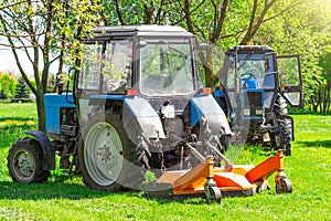 Tractor uses trailed lawn mower to mow grass on city lawns