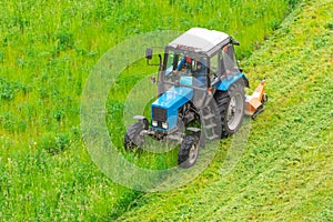 Tractor uses trailed lawn mower to mow grass on city lawns, aerial view