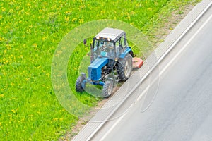 Tractor uses trailed lawn mower to mow grass on city lawns, aerial view