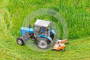 Tractor uses trailed lawn mower to mow grass on city lawns, aerial view