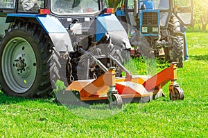 Tractor uses trailed lawn mower to mow grass on city lawns, back view